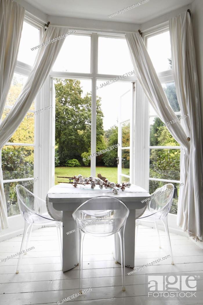 Stock Photo: White table and perspex chairs in bay window with muslin drapes and doors open to the garden | | Designer: Amber Jeavons.