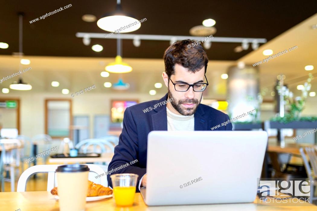 Stock Photo: Portrait of bearded businessman working on laptop in a coffee shop.
