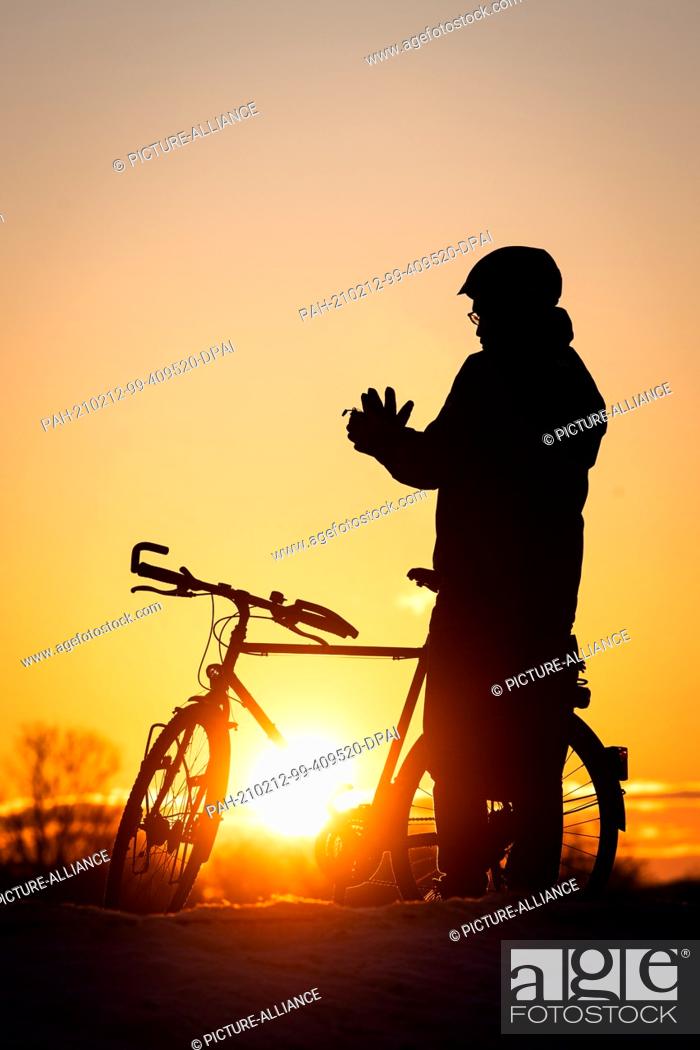 Stock Photo: 12 February 2021, Bremen: A cyclist puts on his gloves at sunrise at Lake Werder. Photo: Sina Schuldt/dpa. - Bremen/Bremen/Germany.