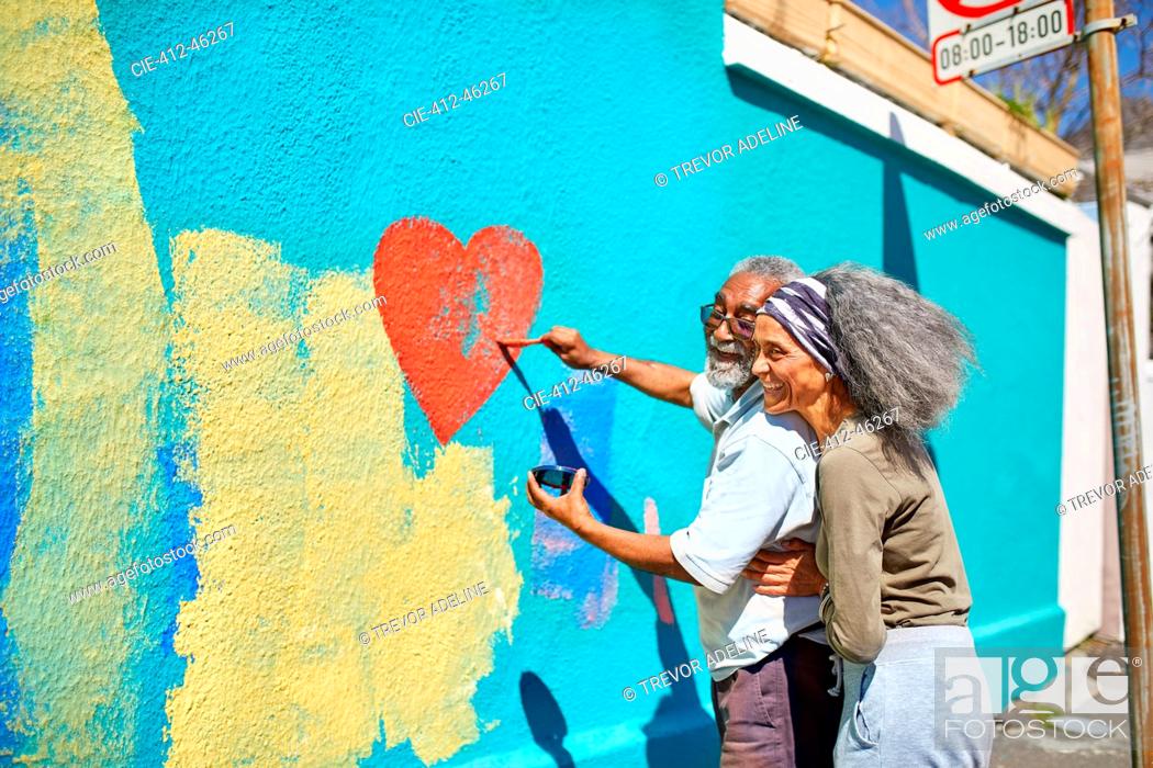 Stock Photo: Happy senior couple painting heart-shape mural on sunny wall.