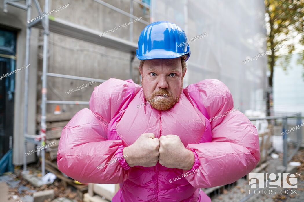 Stock Photo: Portrait of man wearing pink bodybuilder costume and hard hat at construction site.