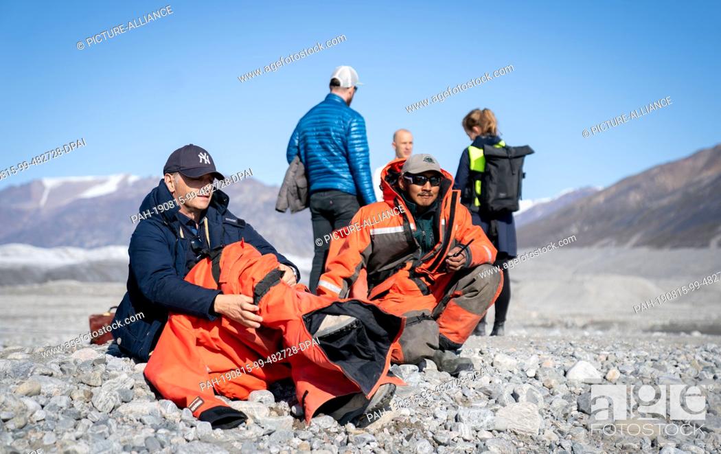 Stock Photo: 15 August 2019, Canada, Pond Inlet: Heiko Maas (l, SPD), German Foreign Minister, puts on a survival suit for the crossing by boat after a glacier tour near.