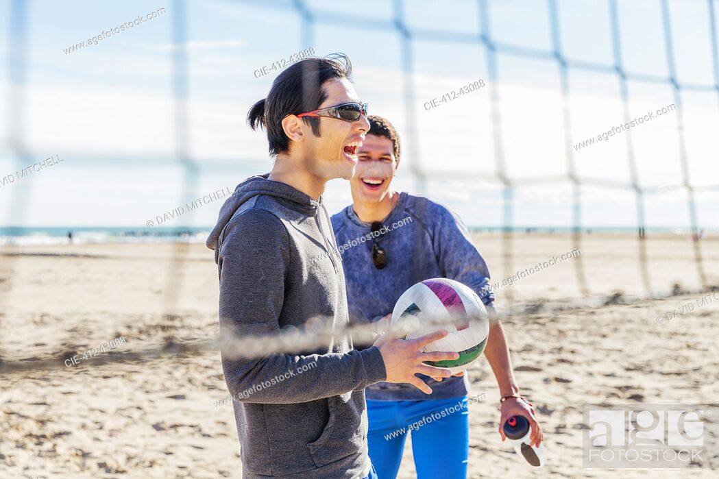 Stock Photo: Happy male friends playing beach volleyball on sunny beach.