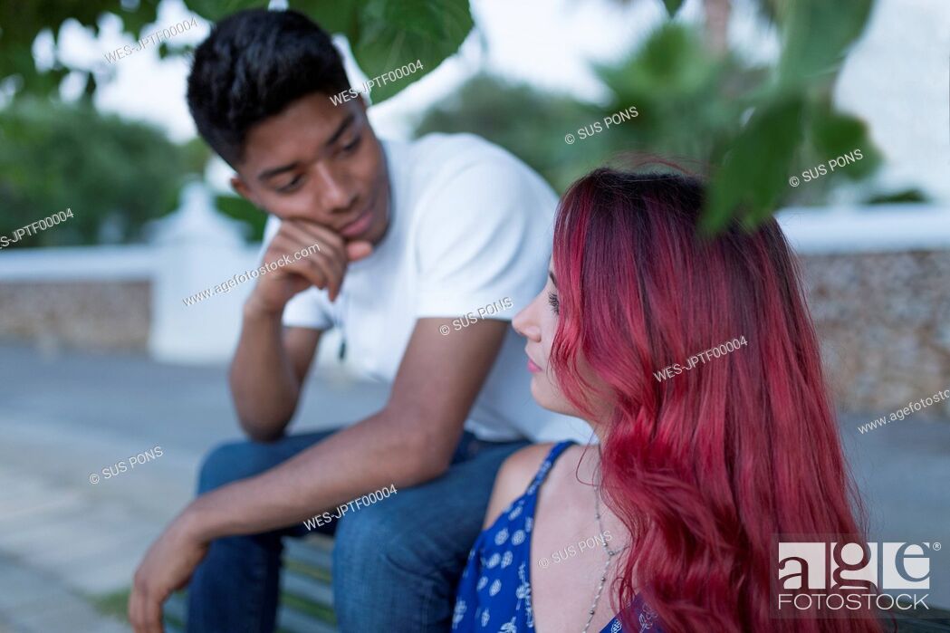 Stock Photo: Young woman with dyed red hair sitting on bench with her boyfriend.