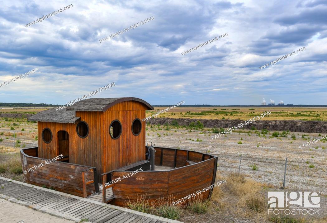 Stock Photo: 15 August 2019, Brandenburg, Cottbus: A small wooden ship stands symbolically at the edge of the former open-cast lignite mine Cottbus-Nord.