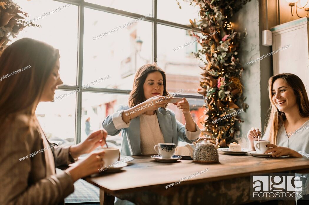 Stock Photo: Young woman with friends taking a photo of cake and tea in a cafe.
