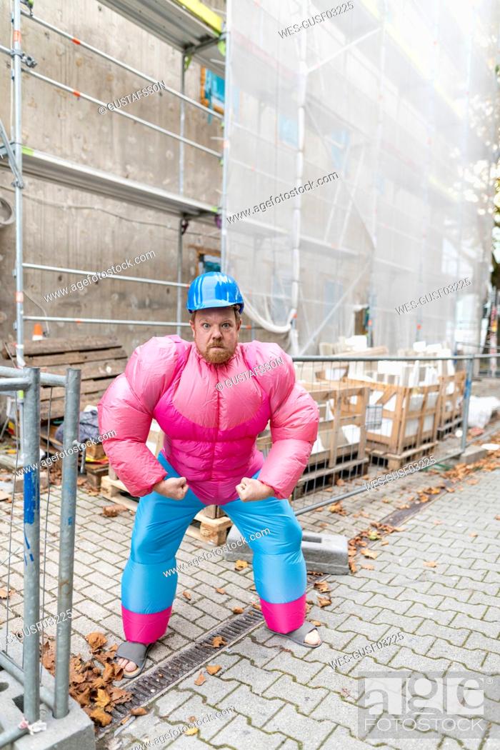 Stock Photo: Portrait of man wearing pink bodybuilder costume and hard hat at construction site.