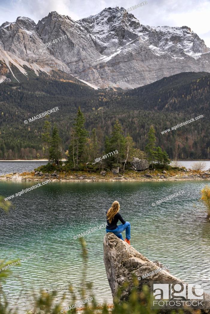 Stock Photo: Young woman sitting on a rock on the shore, view into the distance, Eibsee lake in front of Zugspitzmassiv with Zugspitze, Wetterstein range, near Grainau.