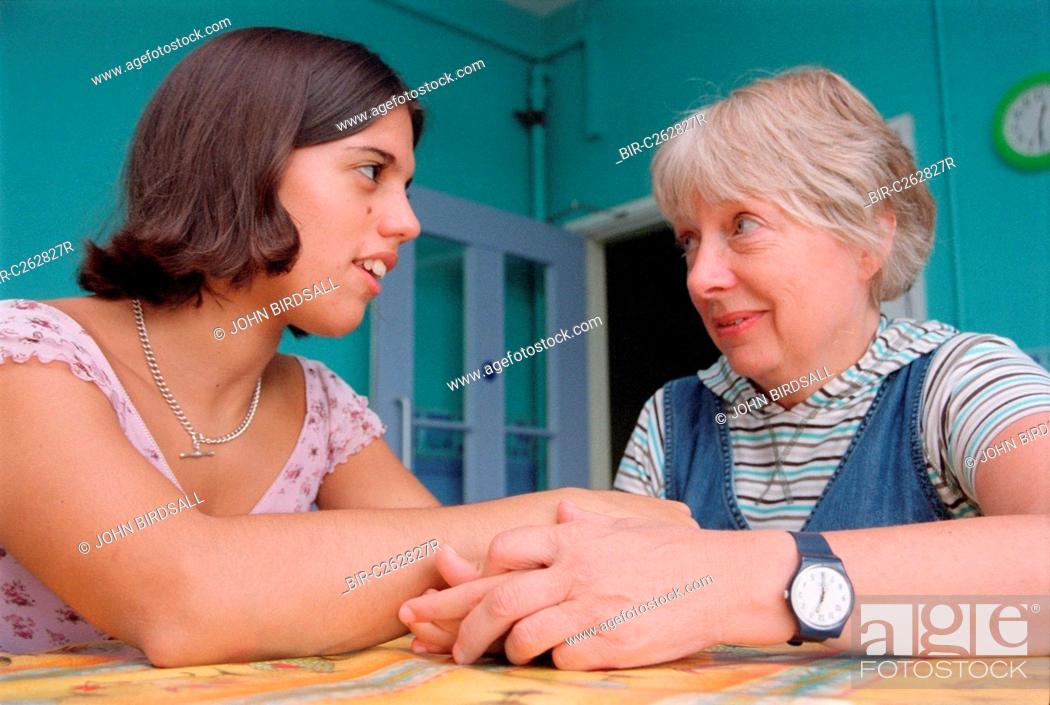 Stock Photo: Teenage girl with physical disability sitting at kitchen table in residential respite care home holding hands and talking with carer,.