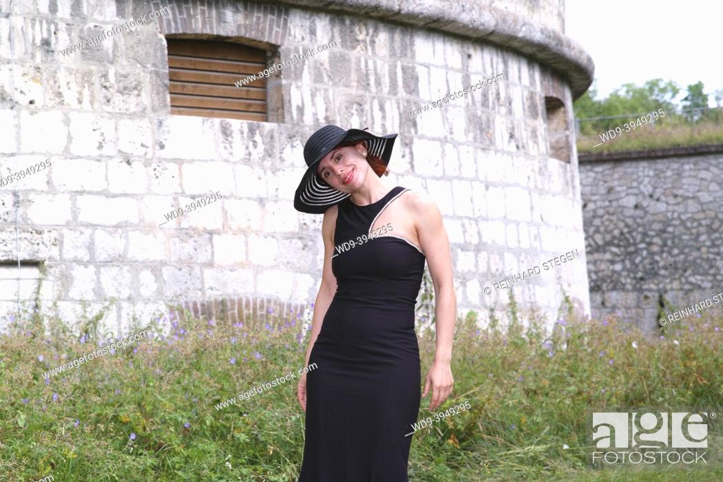 Stock Photo: young woman in form-fitting black dress, with happy face, portrayed against fortress walls.