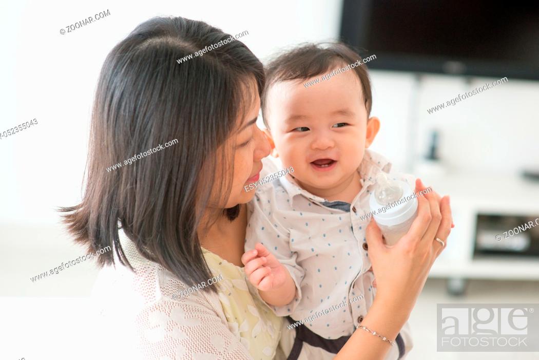Stock Photo: Mother holding milk bottle with happy 9 months old baby. Asian family at home, living lifestyle indoors.