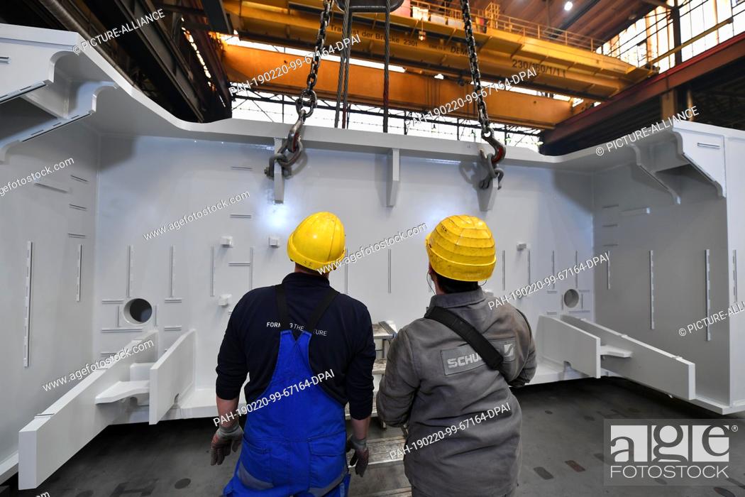 Stock Photo: 20 February 2019, Thuringia, Erfurt: Two employees transport the component of a large press by crane in a production hall of Schuler Pressen GmbH.