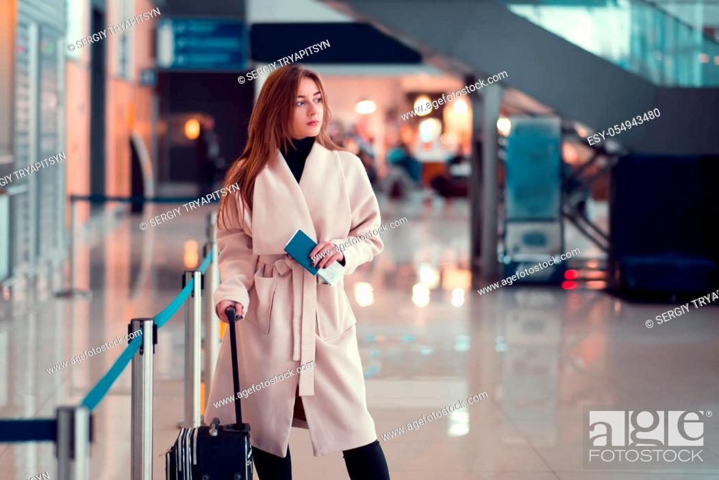 Photo de stock: Young girl standing with a suitcase, holding a passport in the background of escalator at the airport.