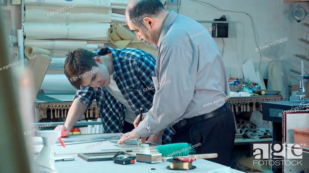 Stock Photo: Senior male worker instructing young trainee how to cut a glass for frame behind the desk in frame workshop. Professional shot in 4K resolution. 083.