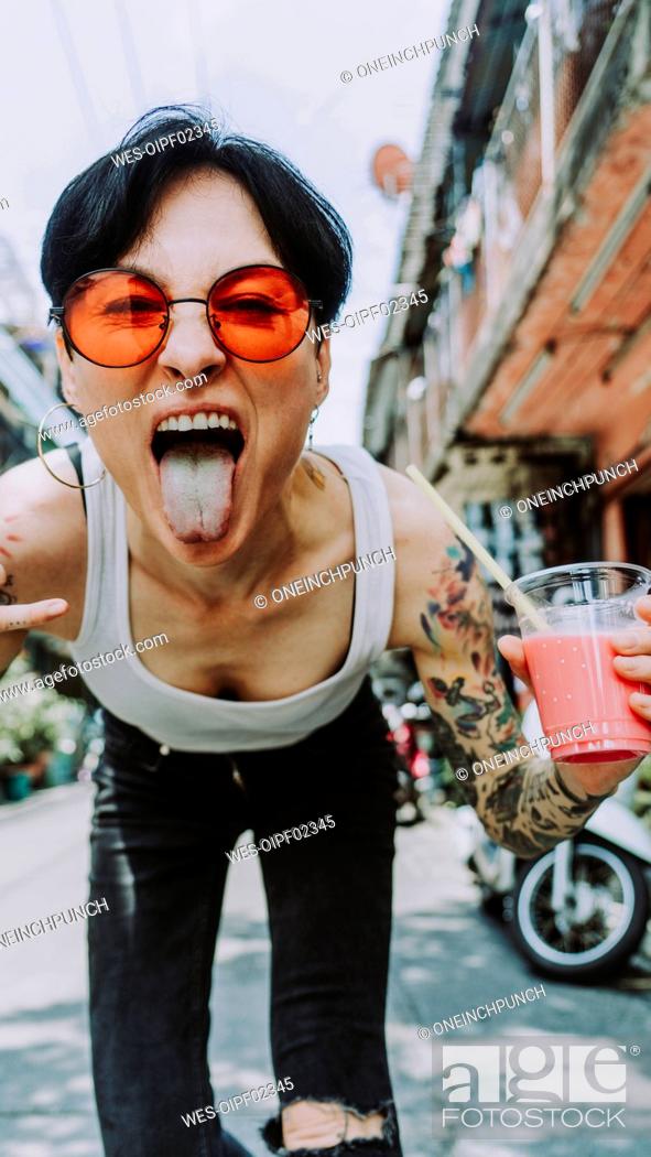 Stock Photo: Tattooed woman sticking out tongue holding glass of drink.