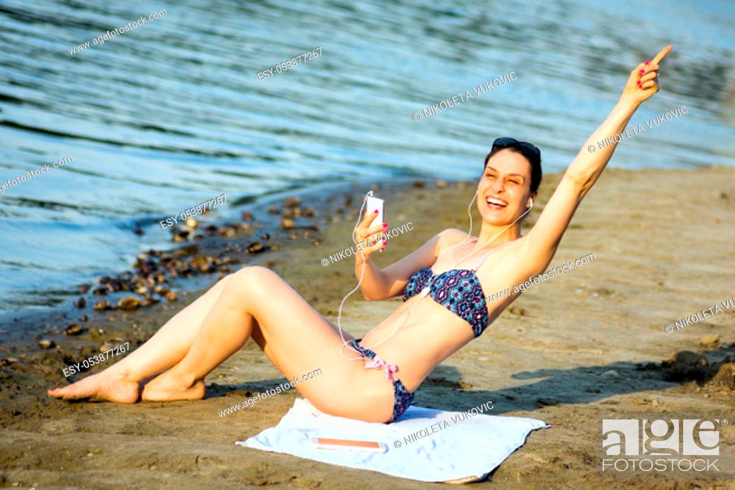 Stock Photo: The attractive cheerful woman in bikini is having fun and using phone on the beach, summer lifestyle.