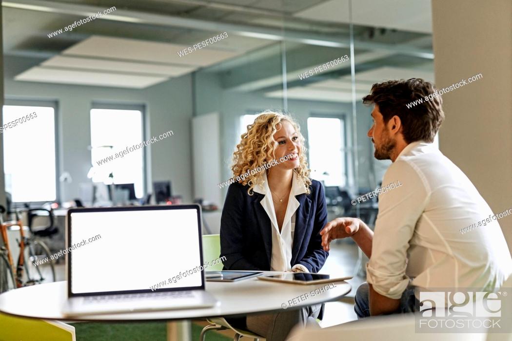 Stock Photo: Two colleagues talking in office with laptop on table.