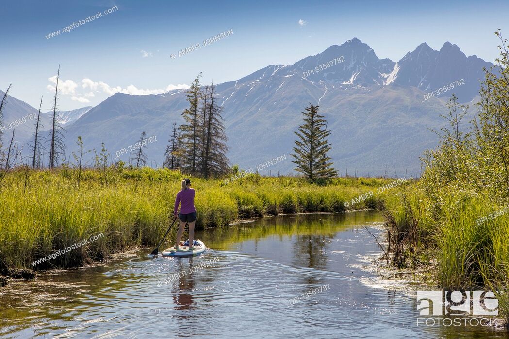 Stock Photo: View from behind of a caucasian woman paddle boarding at Rabbit Slough, towards Twin Peaks in the Chugach Mountains, on a sunny.
