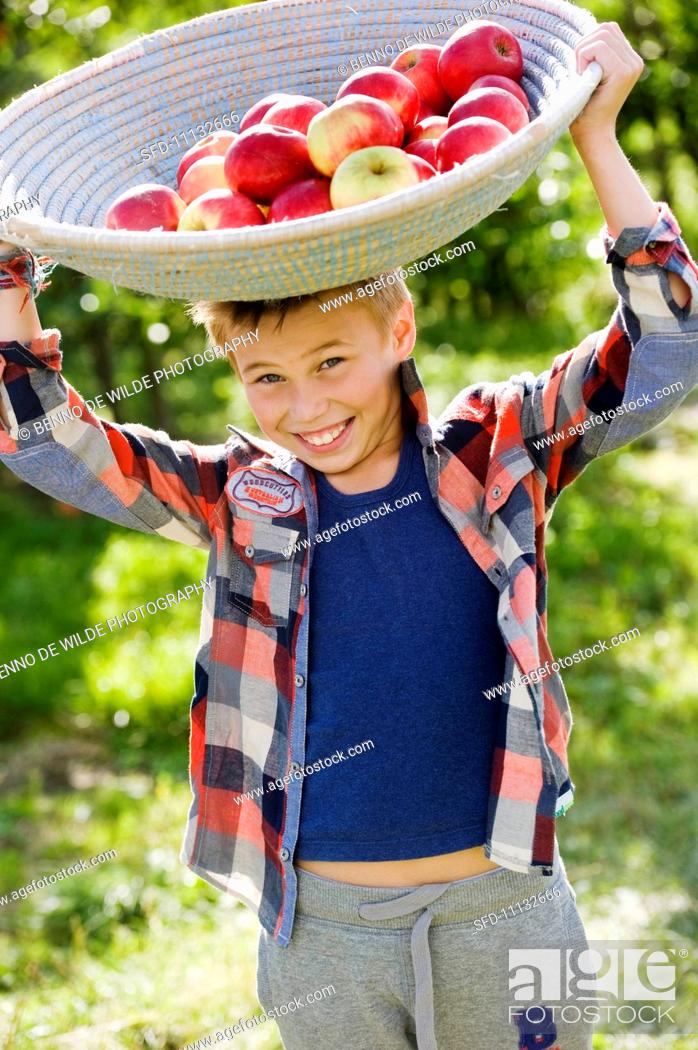 Stock Photo: A boy balancing a basket of apples on his head.