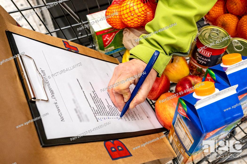 Stock Photo: 26 March 2020, Bavaria, Deggendorf: A helper checks off a shopping list of food. Helpers get food for the elderly and sick.