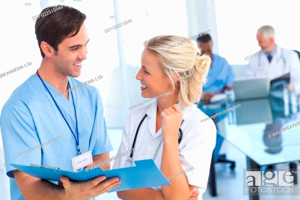 Stock Photo: Two young doctors talking about a blue file in front of two doctors.