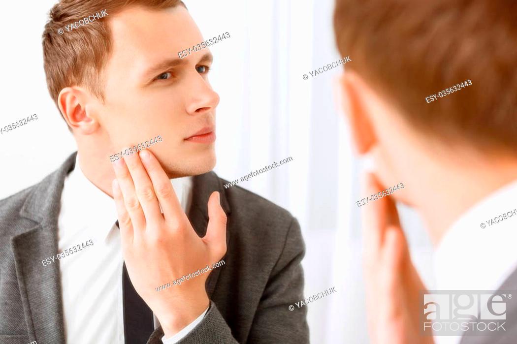 Stock Photo: Intent glance. Handsome young man looking in mirror and checking his bristle hair on face.