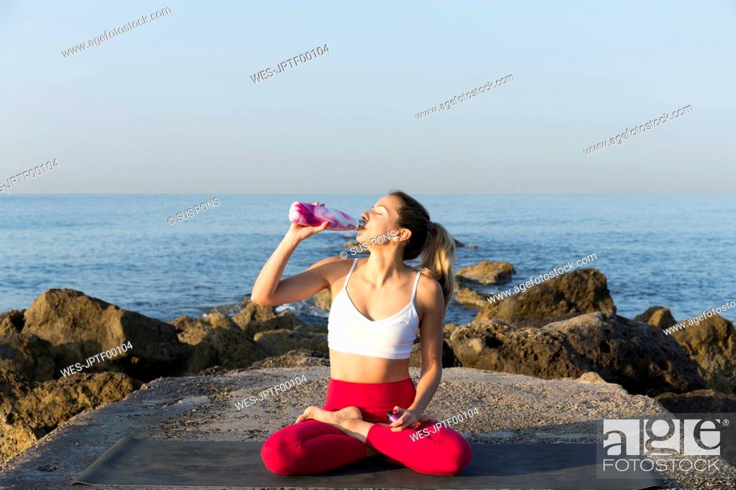 Stock Photo: Young woman practicing yoga on the beach, drinking water.