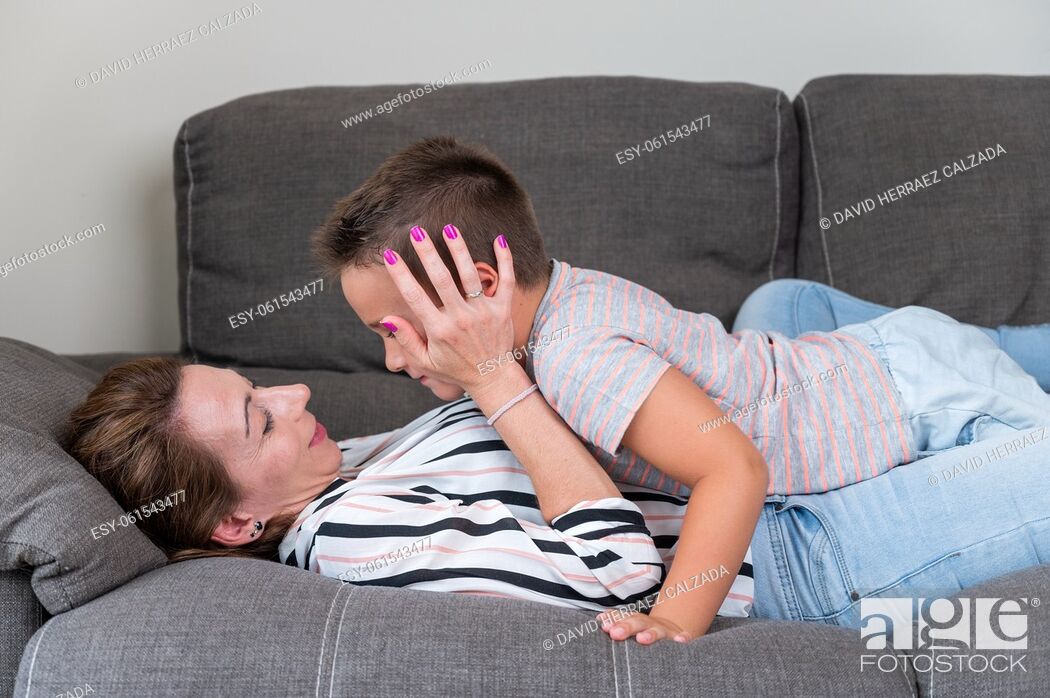Stock Photo: Woman lying on sofa kissing her little son in cheek. Mom with little boy joyfully spending time in cozy living room at home .
