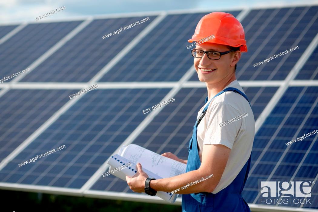 Stock Photo: Young man working with solar panels. Worker at solar power station holding documents looking in camera and smiling.