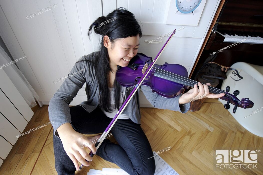 Photo de stock: young asian girl playing the violin in her bedroom in Madrid (Spain).