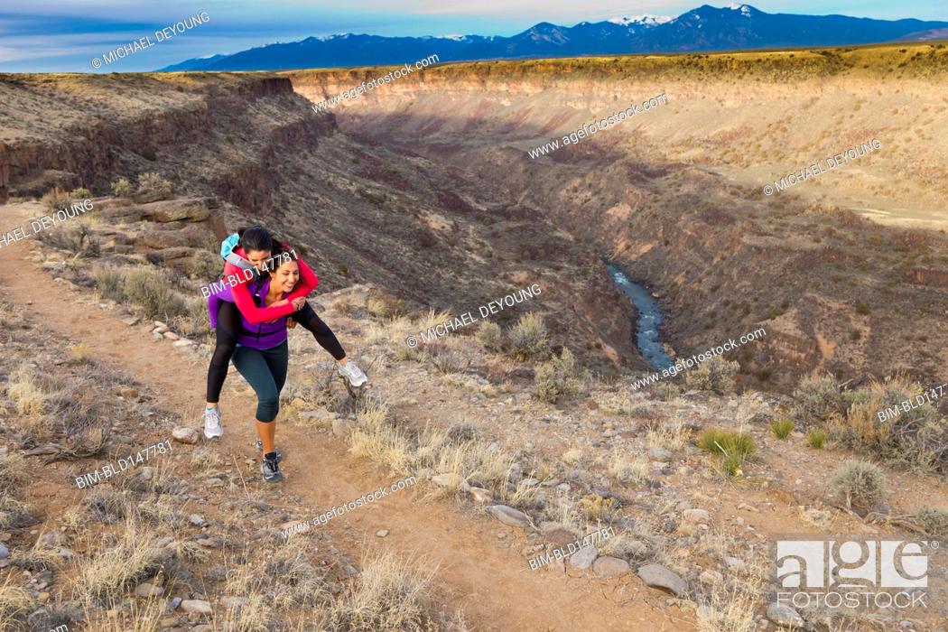 Stock Photo: Hispanic woman carrying friend on her back in remote area.