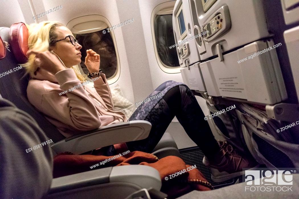Stock Photo: Sporty casual young blonde caucasian lady watching movie while traveling by airplane by the window. Commercial transportation by planes.