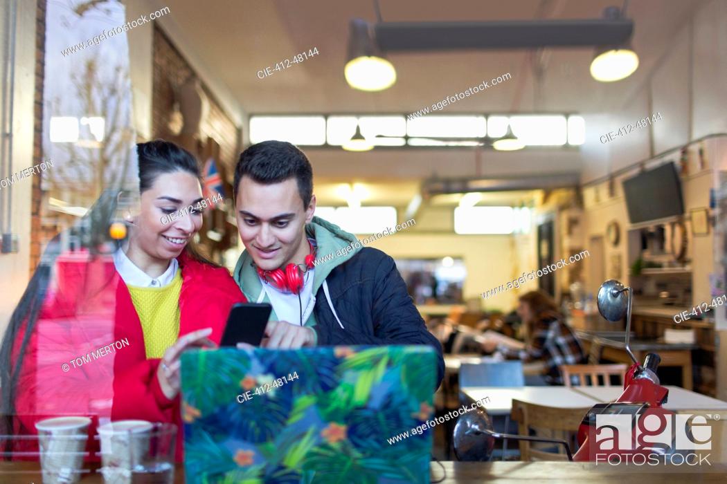 Stock Photo: Young couple using smart phone at cafe window.