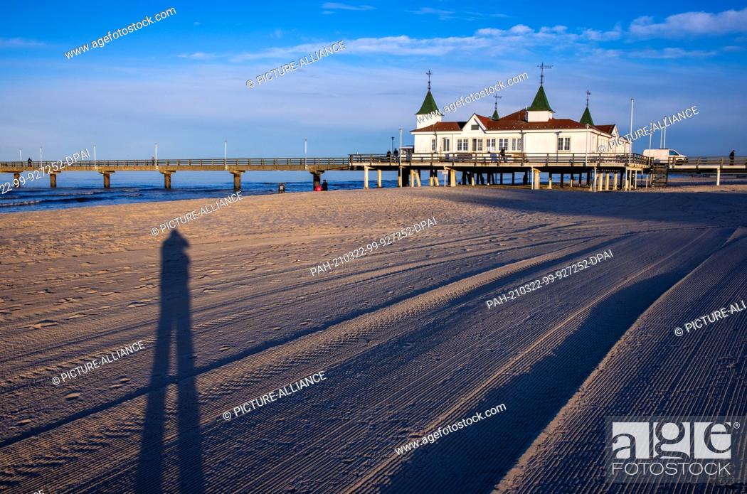 Stock Photo: 22 March 2021, Mecklenburg-Western Pomerania, Ahlbeck: The pier is illuminated on the beach by the setting sun. The weather in northern Germany is sunny but.