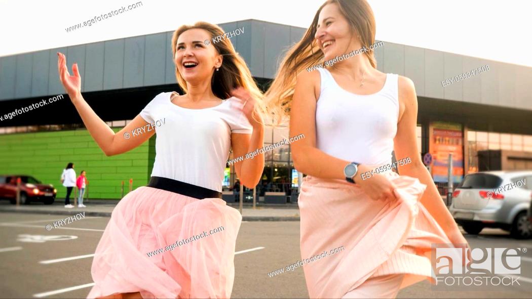 Stock Photo: Portrait of two laughing cheerful girls in same outfit playing and having fun on car parking at shopping mall.