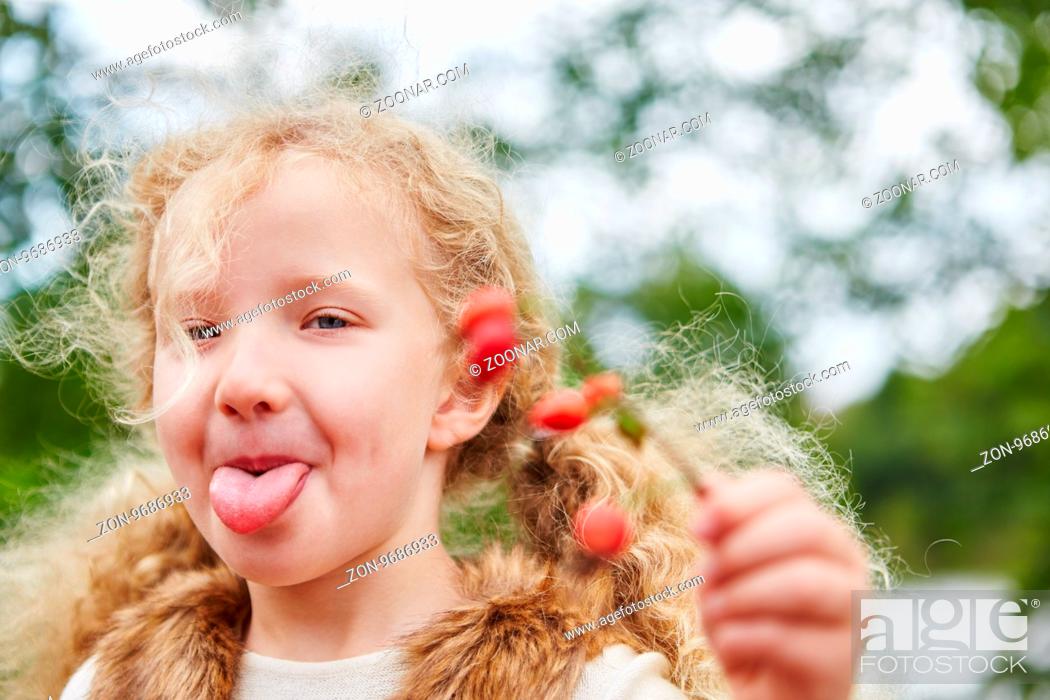 Stock Photo: Mädchen streckt frech die Zunge raus beim Hagebutten pflücken im Herbst.