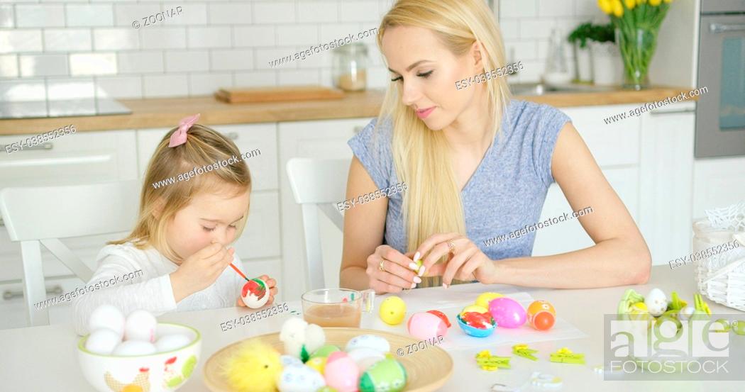 Imagen: Mother looking at girl coloring eggs.