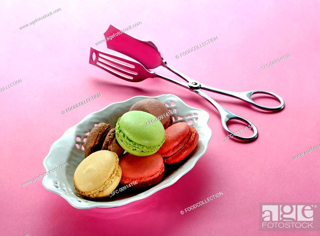Stock Photo: Different types of macaroons in a porcelain dish with a pair of tongs next to it.