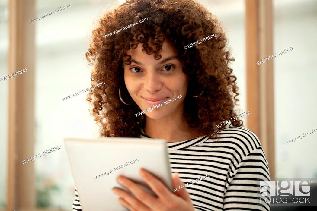Photo de stock: Young adult woman looking at the camera while using digital tablet.