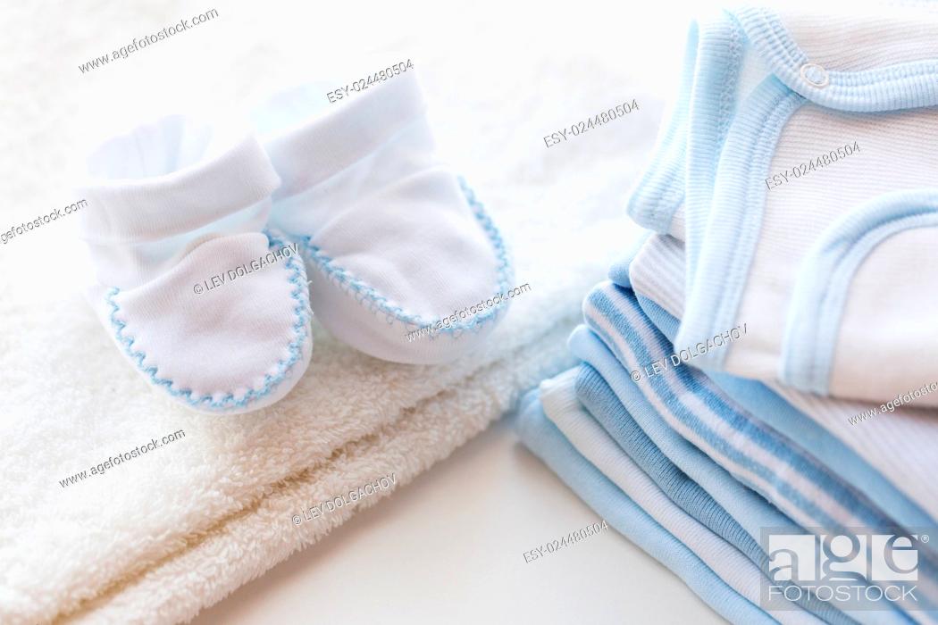 Stock Photo: clothing, babyhood, motherhood and object concept - close up of white baby bootees with pile of clothes for newborn boy.