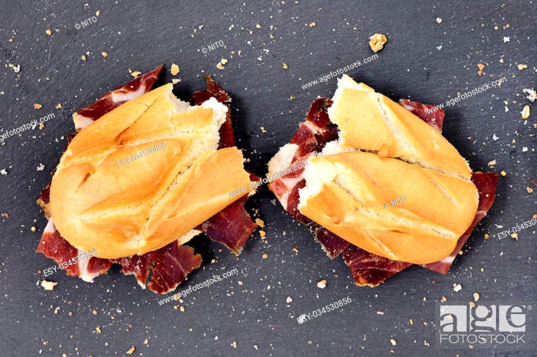 Stock Photo: high-angle shot of a spanish bocadillo de jamon serrano, a serrano ham sandwich, cut in half on a slate stone background.