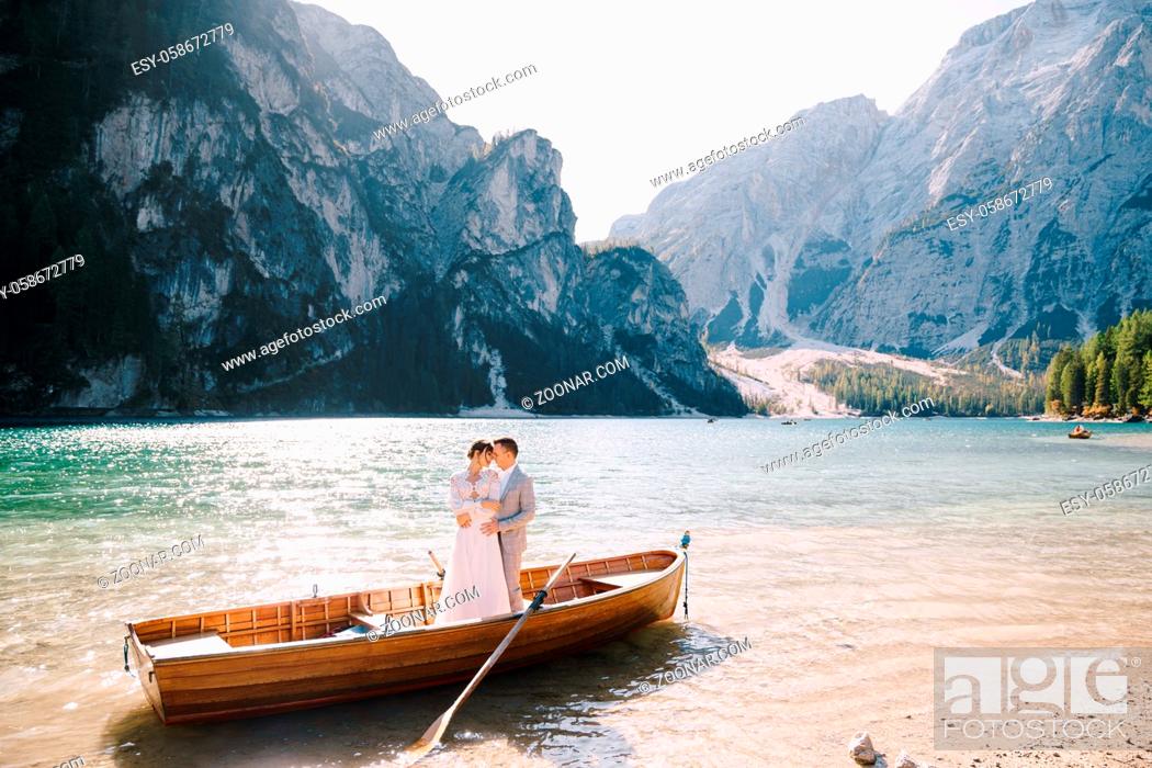 Stock Photo: Bride and groom sailing in wooden boat, with oars at Lago di Braies lake in Italy. Wedding in Europe - Newlyweds are standing embracing in boat.