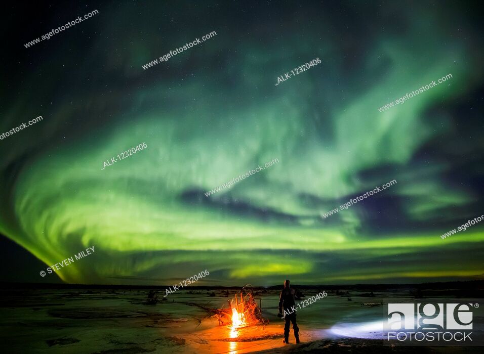 Stock Photo: Man stands next to a campfire while northern lights dance overhead, Delta River, Delta Junction, Interior Alaska, USA.