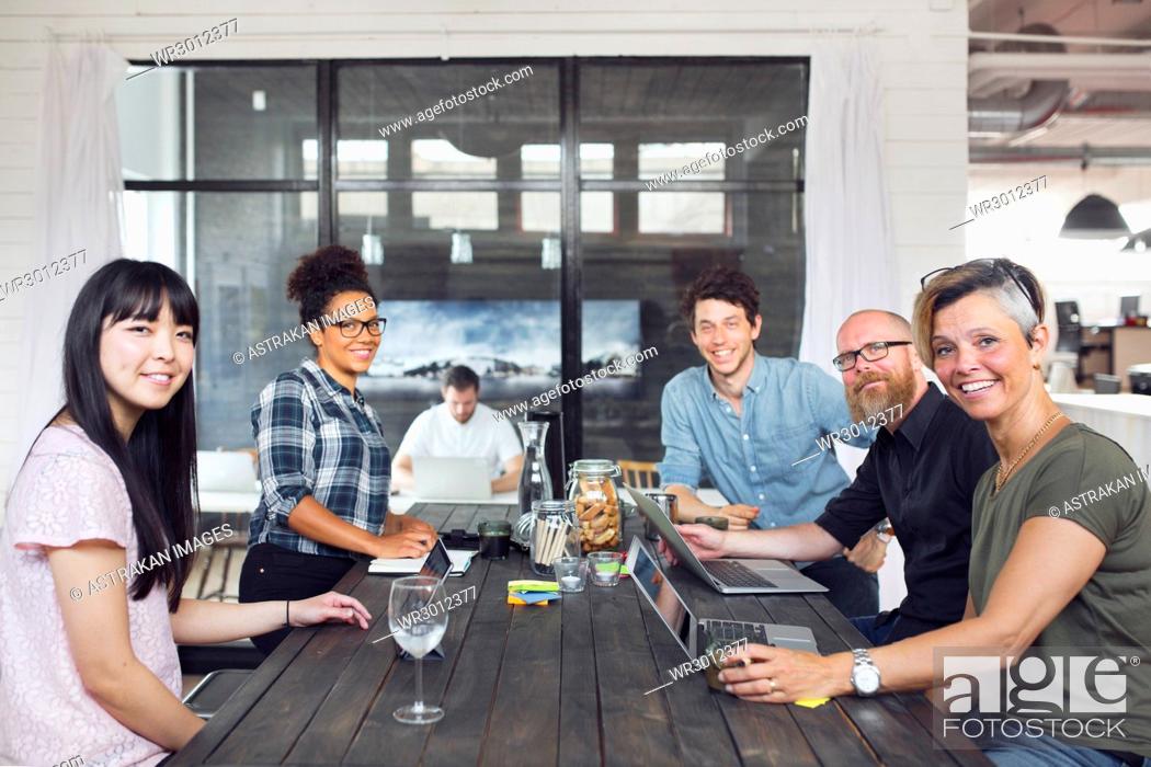 Stock Photo: Group of coworkers looking at camera, one man working in background.