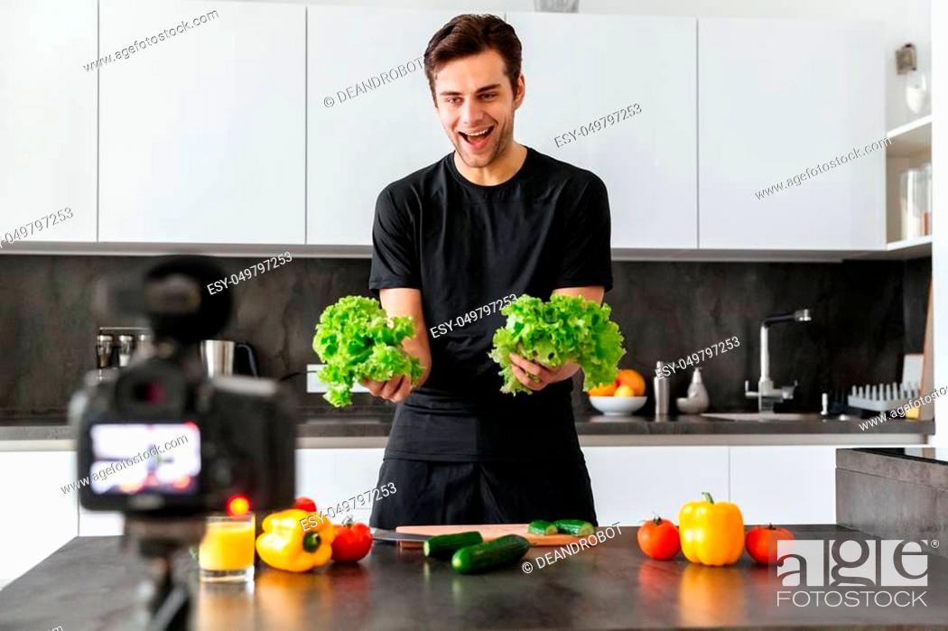 Stock Photo: Cheerful young man filming his video blog episode about healthy food cooking while standing at the kitchen table.