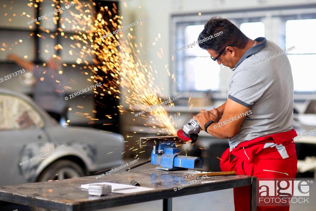 Stock Photo: Mechanic using angle grinder in car workshop.