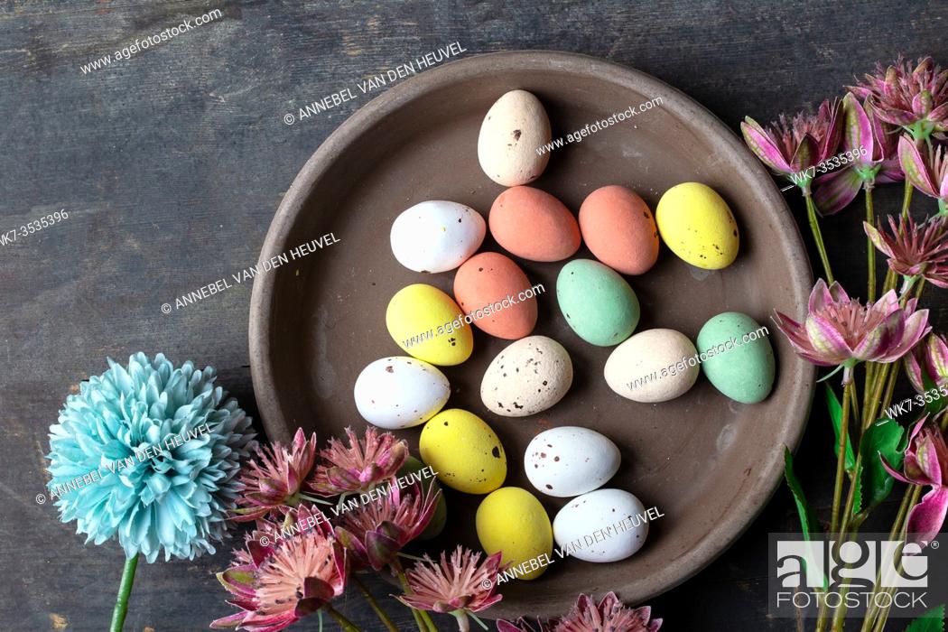 Stock Photo: Easter eggs painted in pastel colors on a vintage wooden background texture, concrete look plate surrounded with various spring flowers in modern colors.
