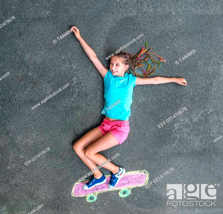 Imagen: cute little girl on a skateboard drawn in chalk on the pavement. view from above.