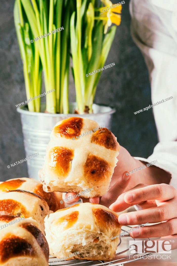 Stock Photo: Child hands take homemade Easter traditional hot cross buns on cooling rack on white marble table with narcissus flowers.