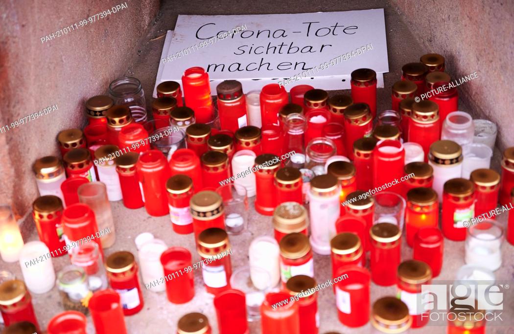 Stock Photo: 11 January 2021, Berlin: ""Making Corona dead visible"" is written on a cardboard box. Several posters, grave lights and candles stand on the pedestal of the.
